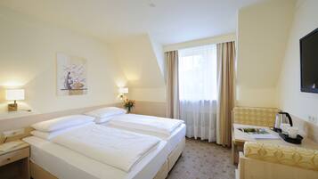 A hotel room with two beds, a desk, a chair, a TV, and a window with curtains.