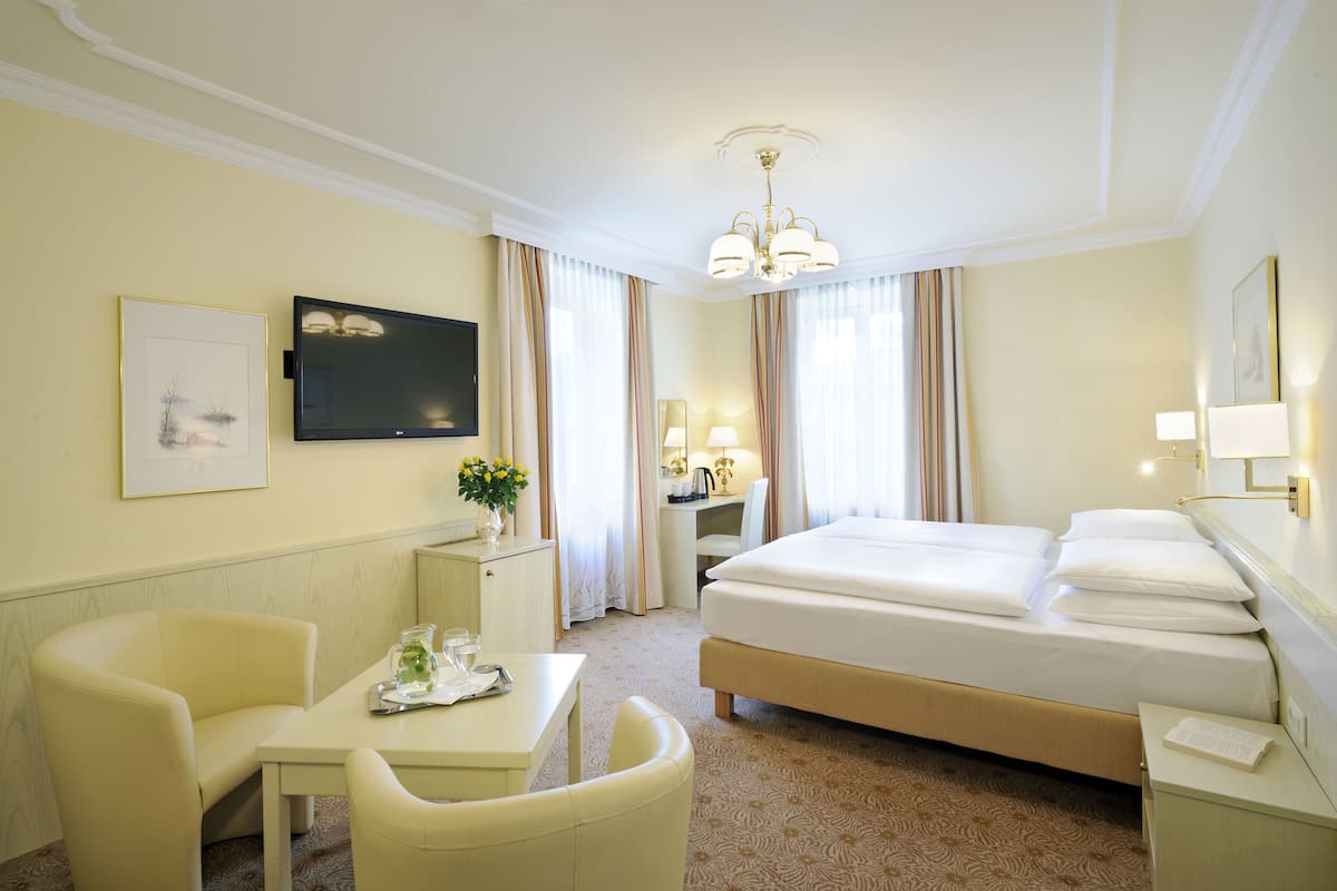 A hotel room with a bed, a desk, a chair, a television, and a window with curtains.