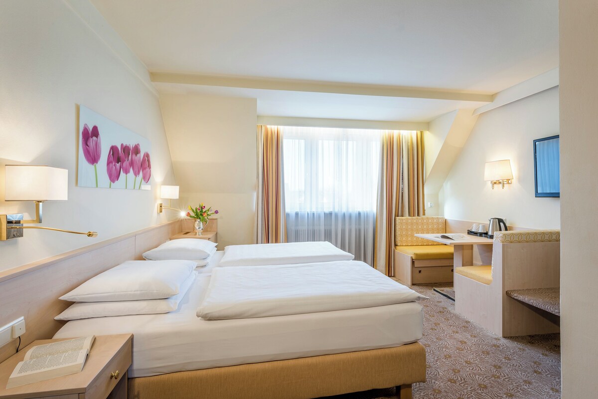 Una habitación de hotel con una cama grande, un escritorio, una silla y una ventana con cortinas.