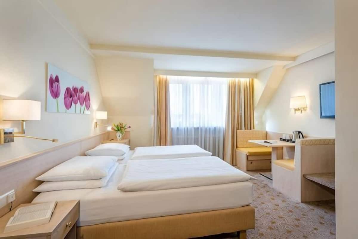 A hotel room with a large bed, a desk, a chair, and a window with curtains.