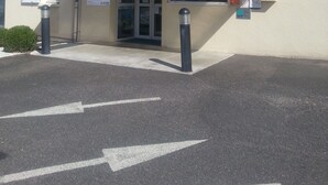 Un hotel llamado 'Tour Hotel' con entrada cubierta, un letrero y una zona de estacionamiento con flechas direccionales.