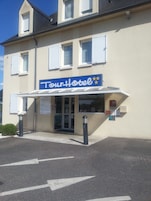 Um hotel chamado 'Tour Hotel' com entrada coberta, placa de identificação e área de estacionamento com setas indicativas.