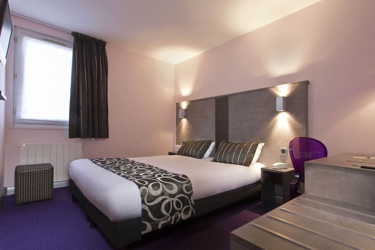 Moderni hotellihuone, jossa on suuri sänky, yöpöydät, työpöytä ja tuoli.