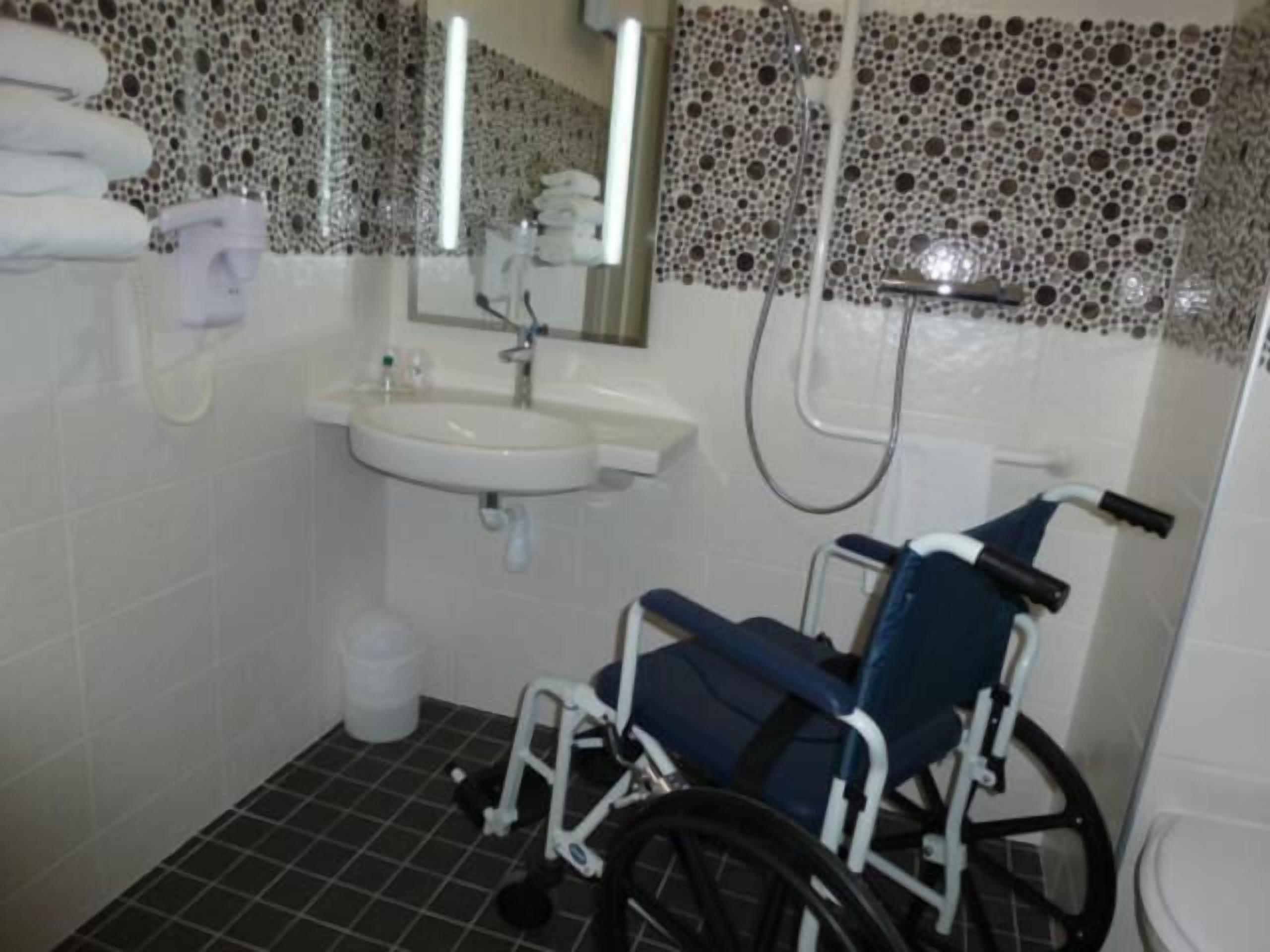 Un baño accesible en silla de ruedas con lavamanos, espejo y ducha.