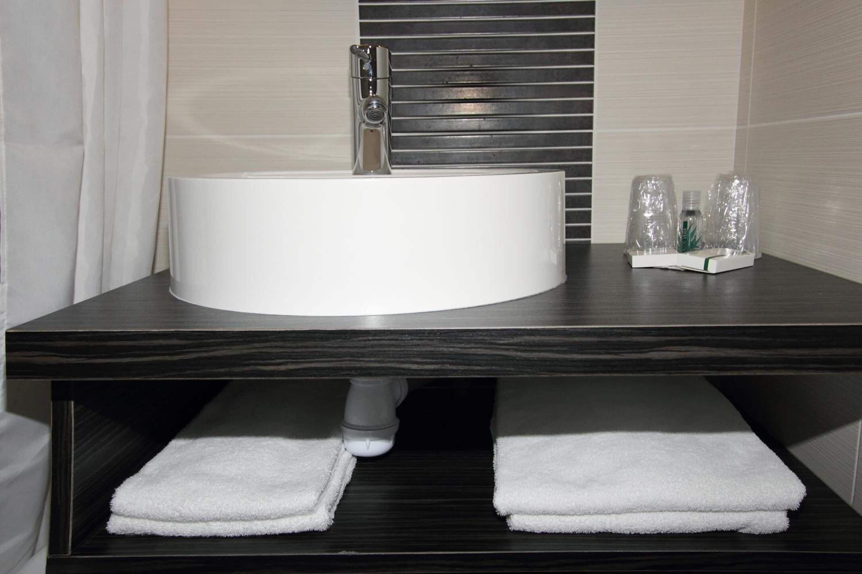 Un baño con un mueble de tocador de madera oscura, un lavabo blanco y dos toallas blancas en la estantería.