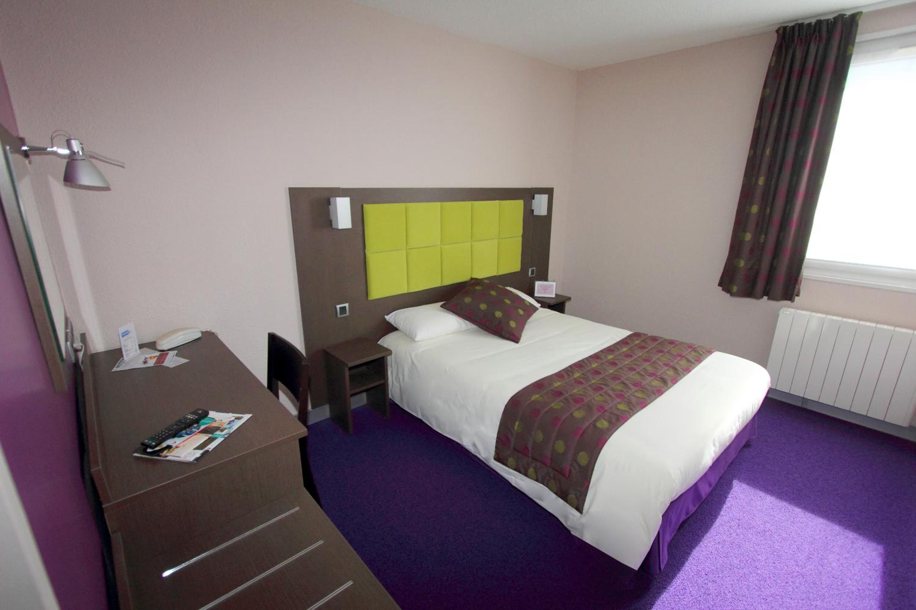 A hotel room with a bed, a desk, and a nightstand.
