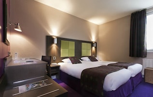 Quarto de hotel com duas camas, uma escrivaninha, uma cadeira e uma mesinha.