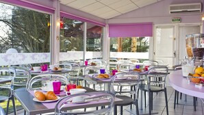 Un café con terraza, mesas con sillas y vistas a árboles y edificios.