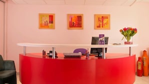 Un mostrador de recepción con decoración roja, una computadora y un florero con flores.