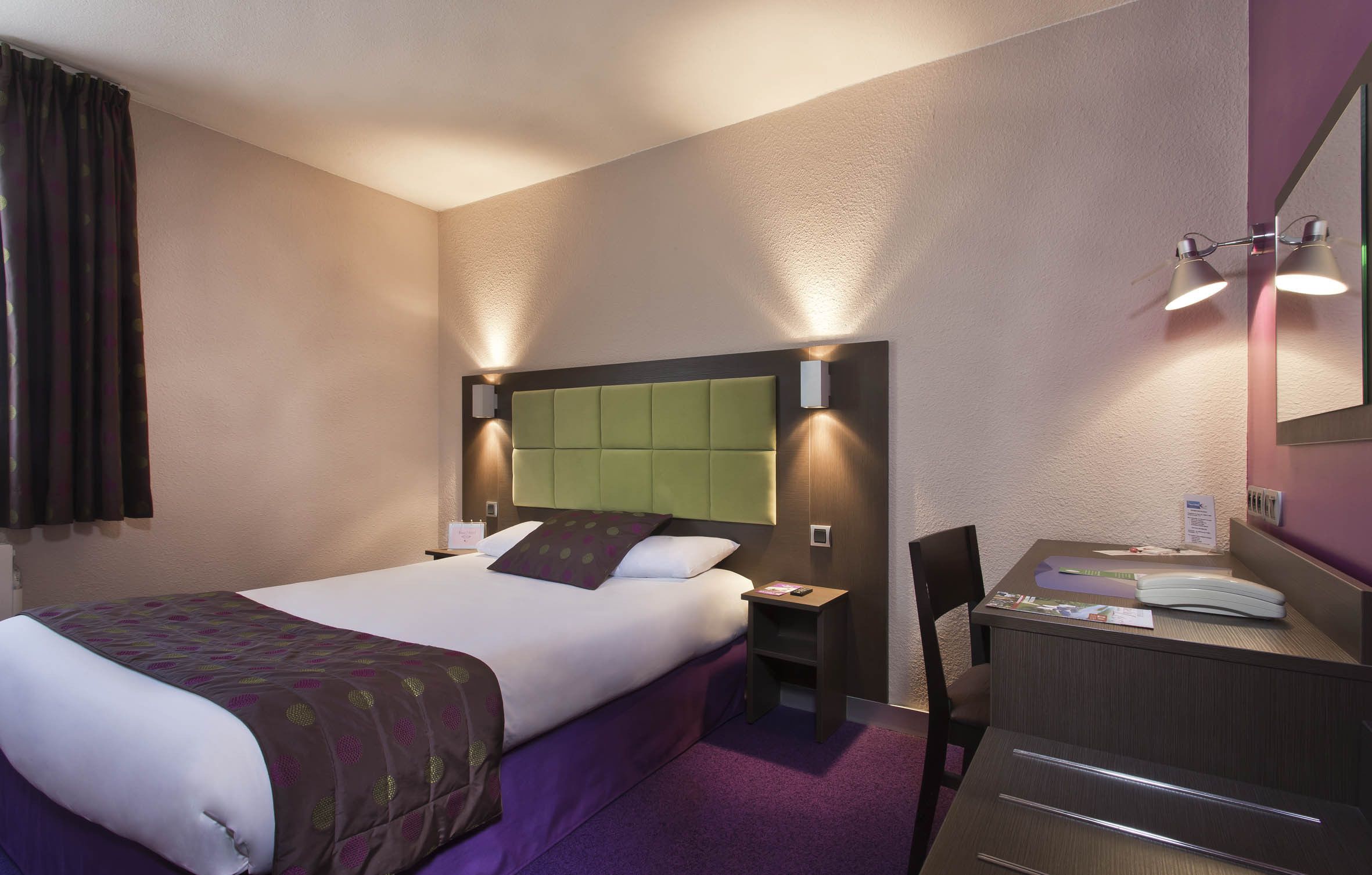 Een hotelkamer met een bed, nachtkastje, stoel, bureau en een spiegel.