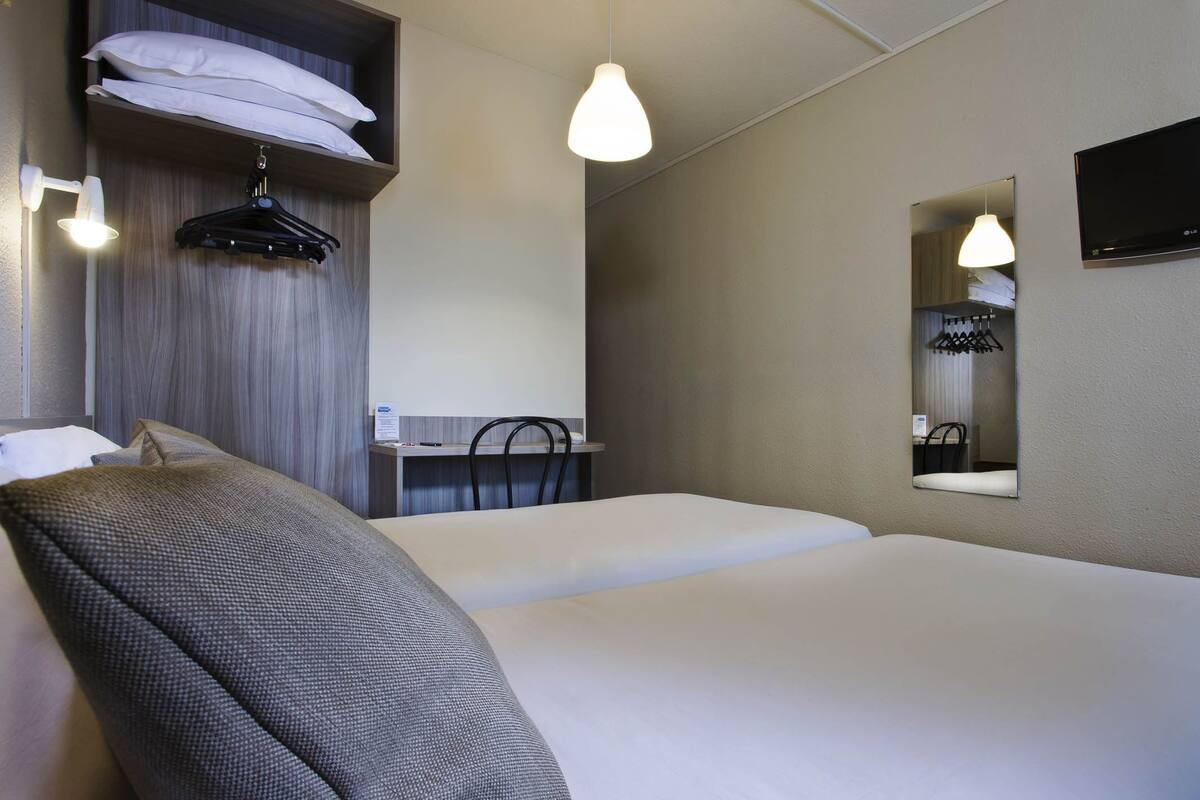 Hotellihuone, jossa on sänky, työpöytä tuolilla, peili ja seinälle ripustettava naulakko.