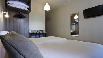 A hotel room with a bed, a desk with a chair, a mirror, and a hanging coat rack.