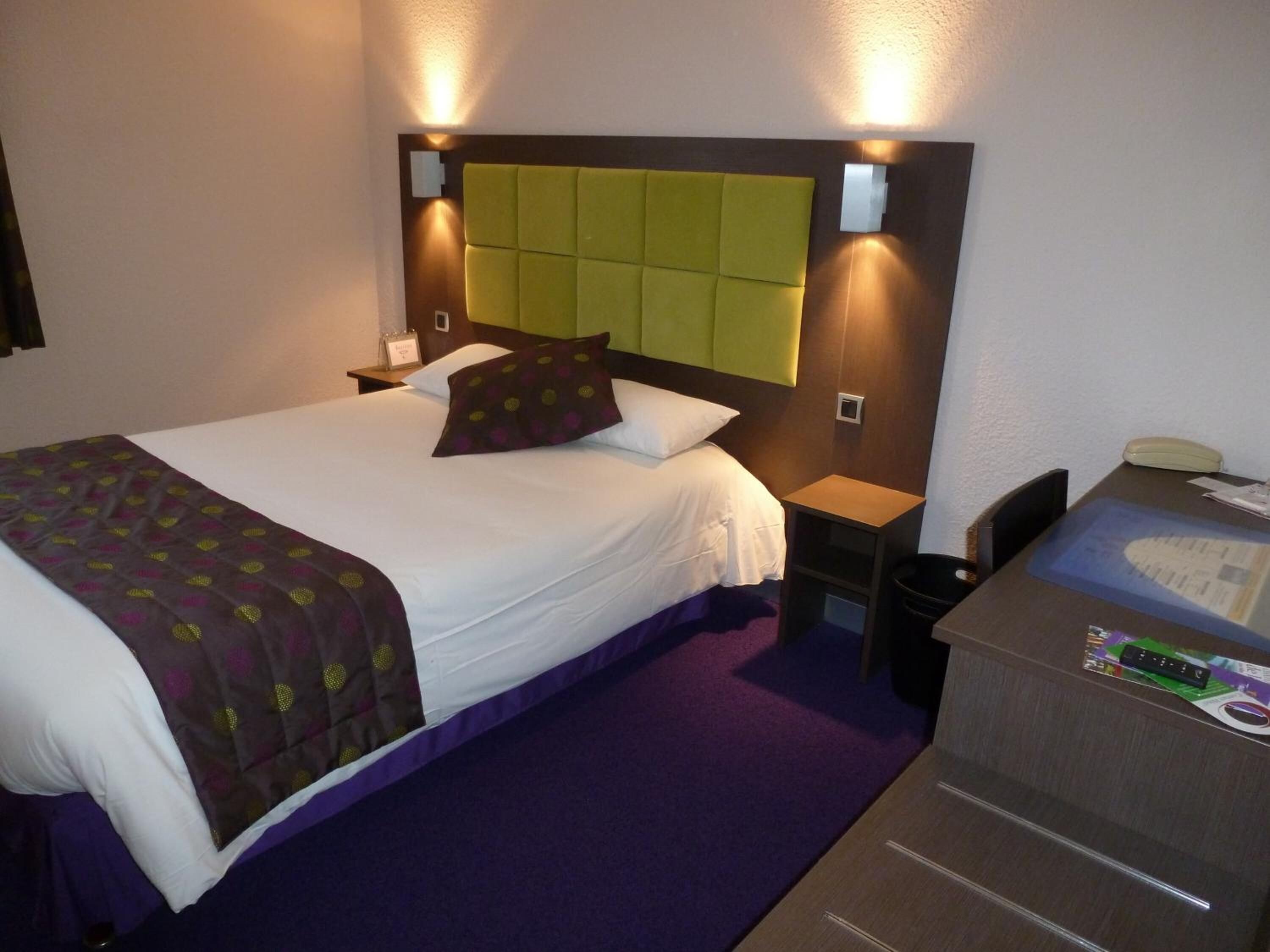 Ein Hotelzimmer mit Bett, Nachttischen, einem Schreibtisch mit Telefon und einem Mülleimer.