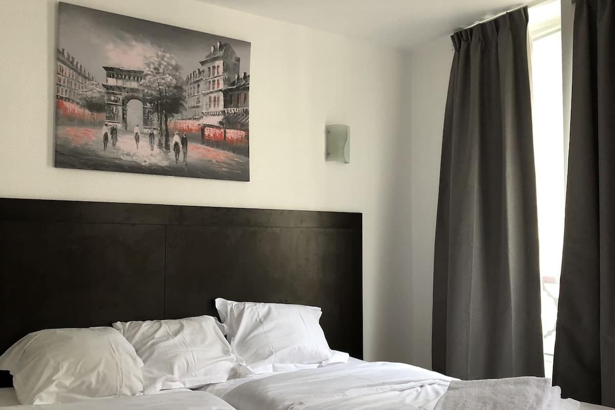 A hotel room with a large bed, two pillows, a headboard, a painting on the wall, and a window with curtains.
