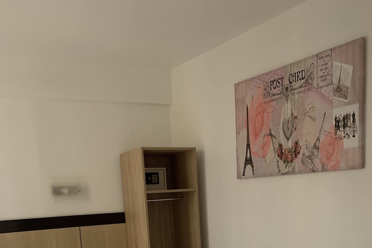 A bedroom with a bed, a wooden wardrobe, and a wall-mounted artwork depicting the Eiffel Tower.