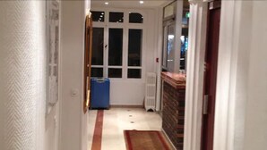 Un pasillo estrecho con un radiador, una maleta azul y una puerta que da a una habitación.