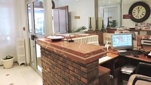 Un mostrador de recepción con encimera de ladrillo, una computadora y un reloj en la pared.