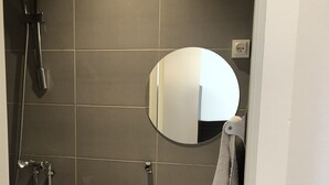 Un baño con lavamanos blanco, un espejo redondo y un cabezal de ducha.