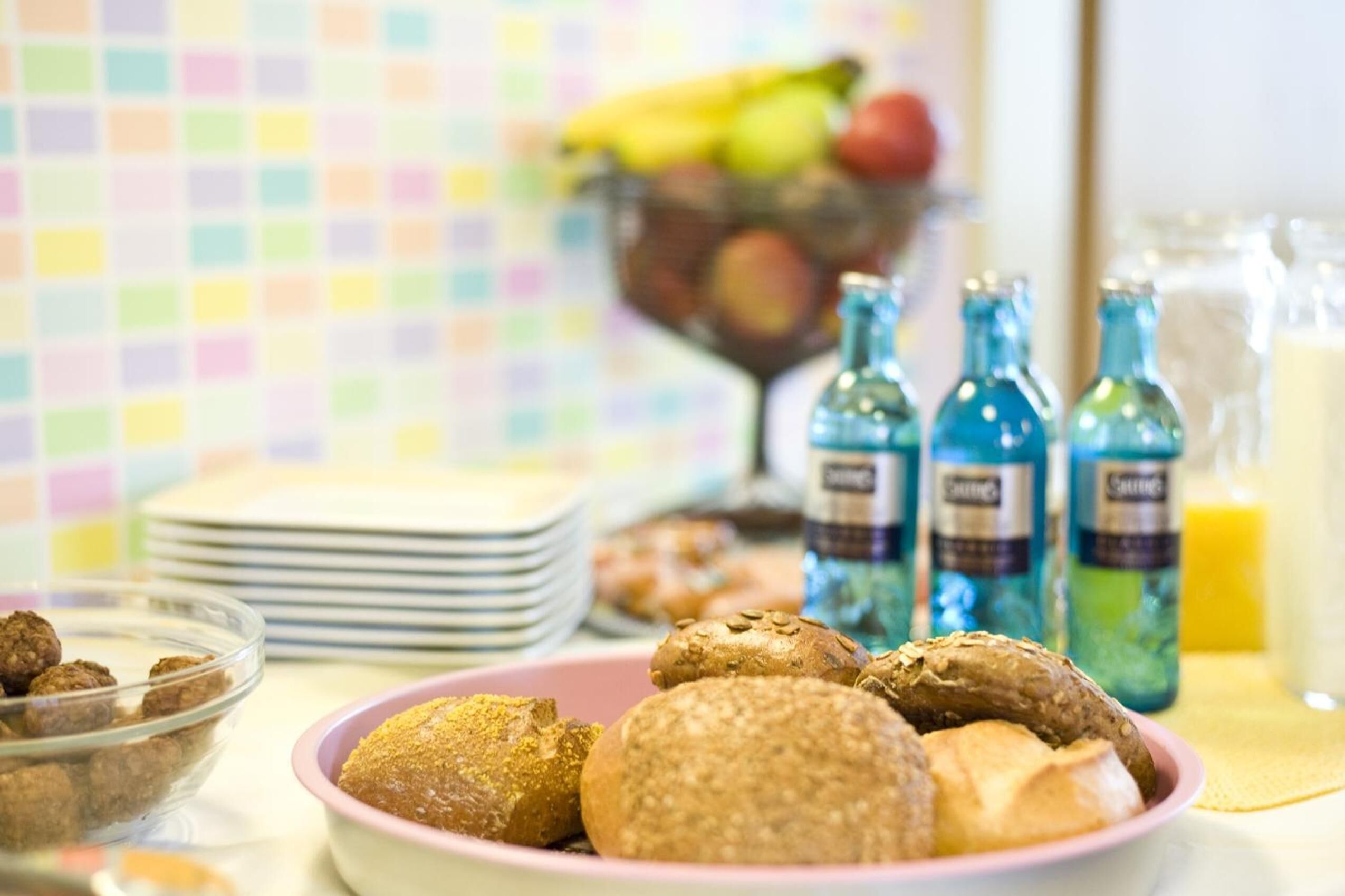 Uma mesa de café da manhã com um prato de biscoitos, uma travessa de doces e uma cesta de frutas ao fundo.