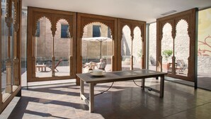 A spacious room with a large table and chairs, a view through a glass door to an outdoor area with a bench and umbrella, and a stone wall in the background. - Onix Liceo (Barcelona)