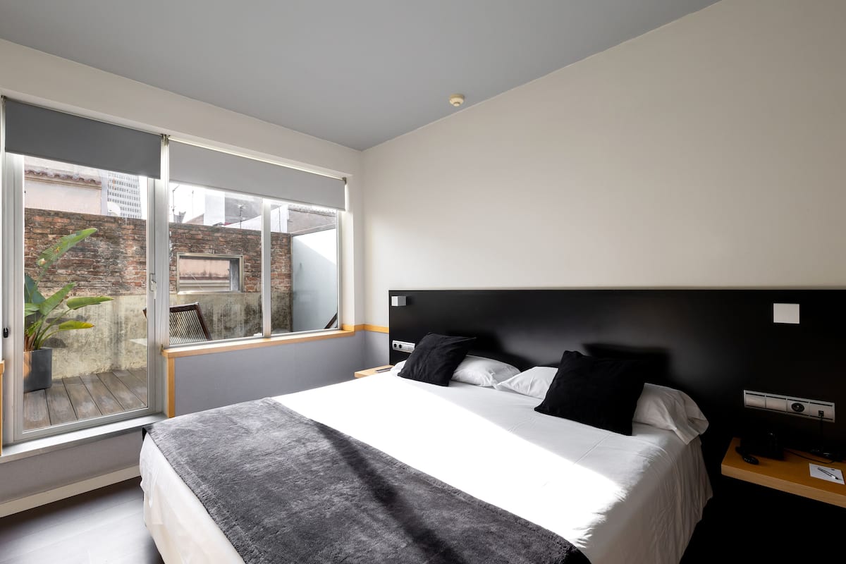 Una habitación de hotel moderna con una cama grande, una mesita de noche, un escritorio y un ventanal corredero que da a un espacio exterior.