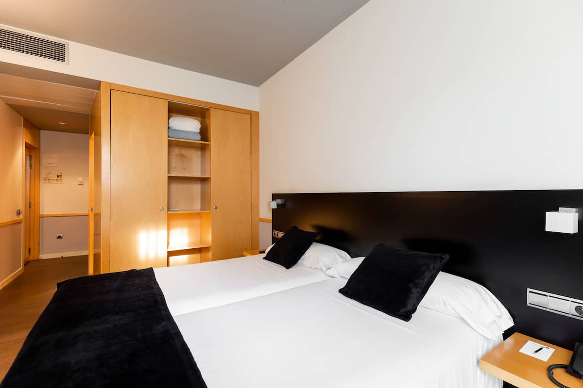 Habitación de hotel con una cama grande, un armario de madera y una mesita de noche con teléfono.