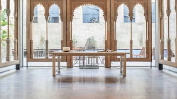 A spacious room with a large wooden table, ornate wooden doors, and a view of a courtyard with a pool.