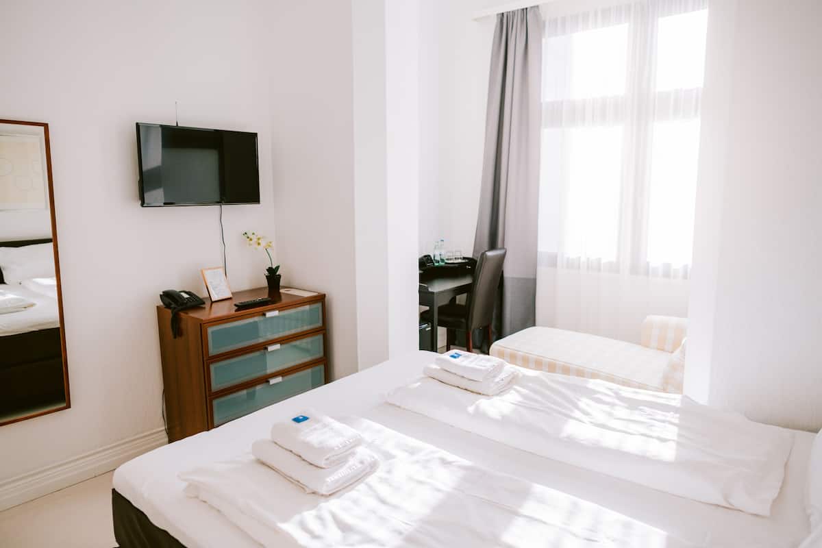 Habitación de hotel con cama, escritorio, silla, televisor y ventana con cortinas.