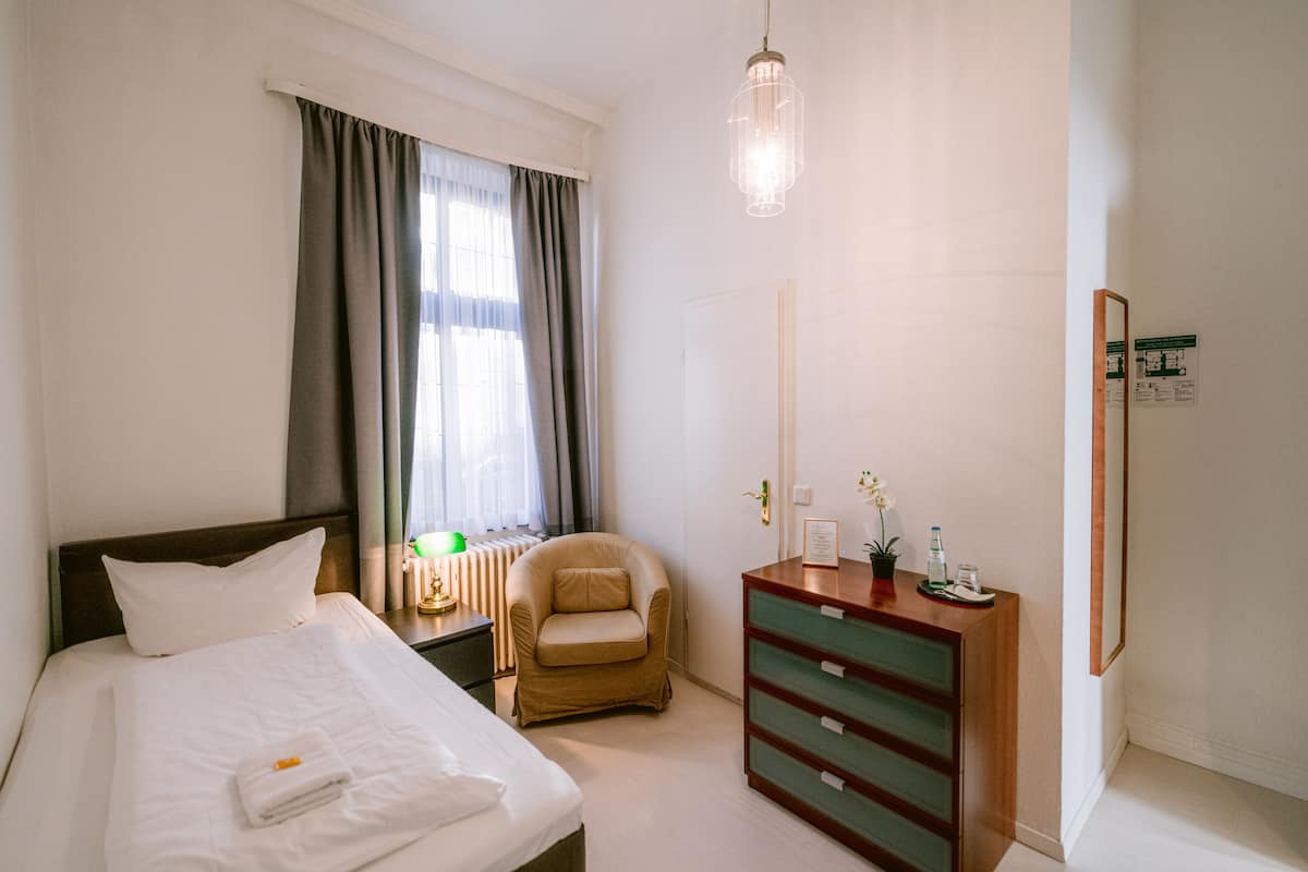 Habitación de hotel con cama, una silla, cómoda y ventana con cortinas.