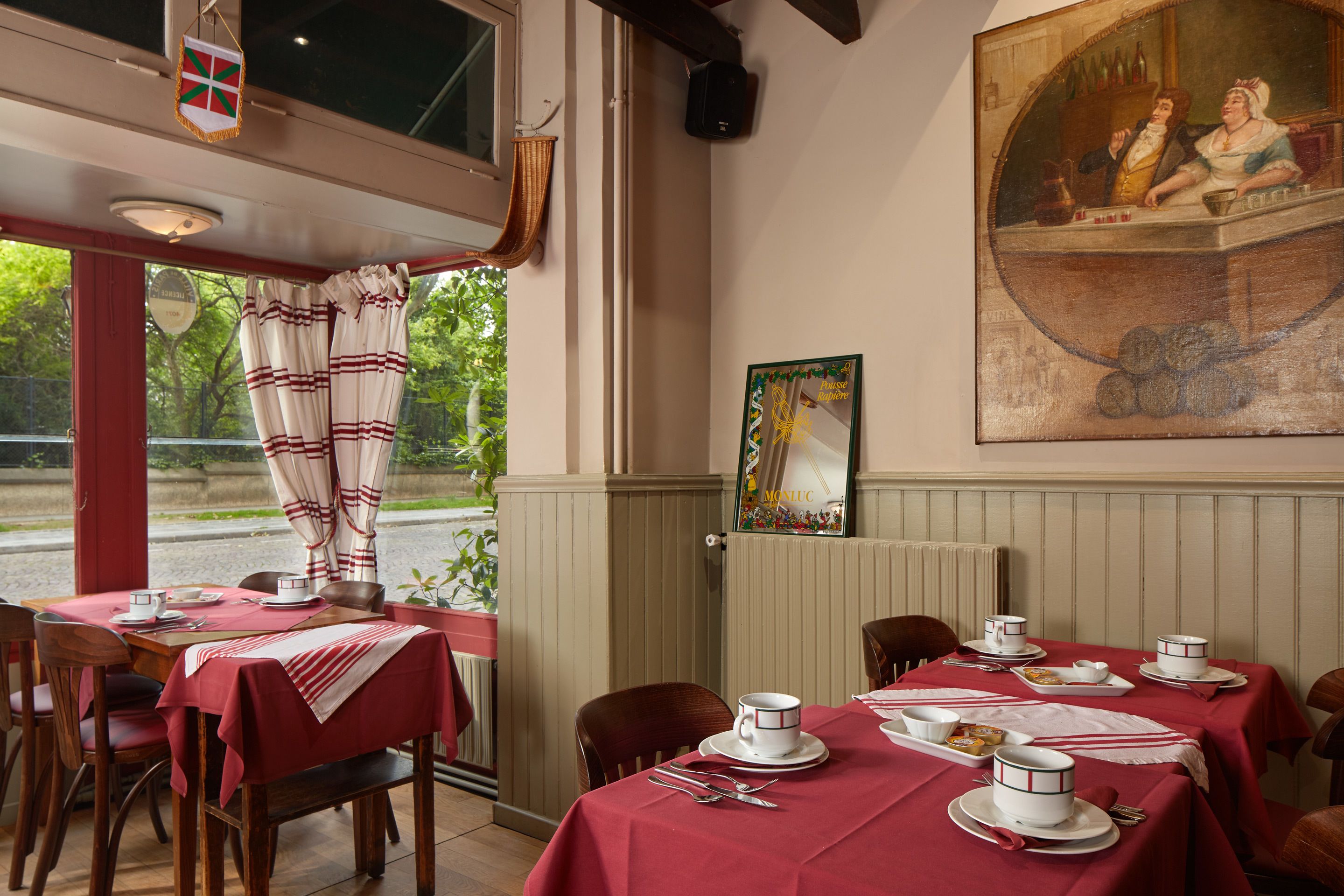 Un coin repas avec des tables dressées pour le repas, un tableau accroché au mur et une fenêtre avec des rideaux.