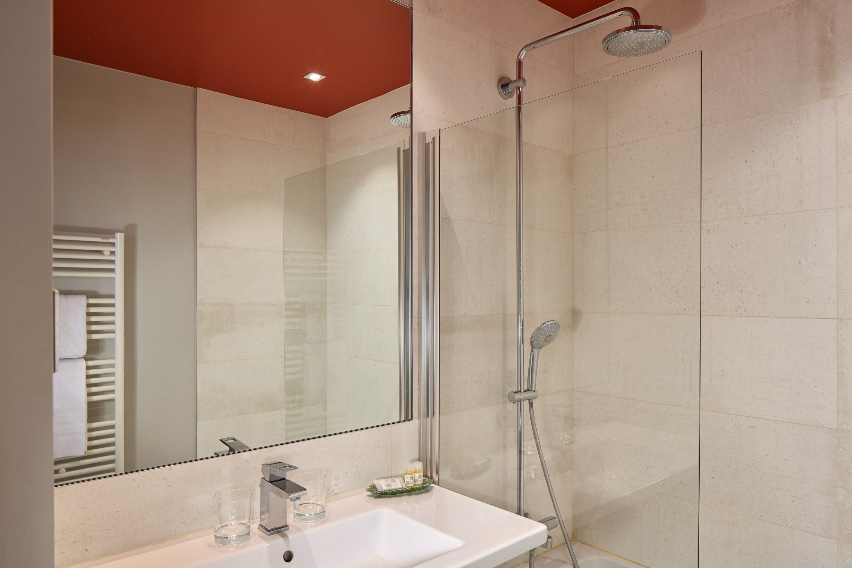 Un baño moderno con ducha envuelta en vidrio, un lavamanos blanco y un espejo grande.