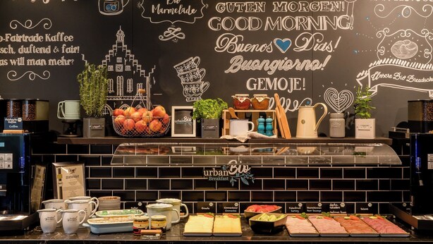 Una barra de desayuno con una pared de pizarra que muestra diferentes opciones para el desayuno y saludos en varios idiomas.