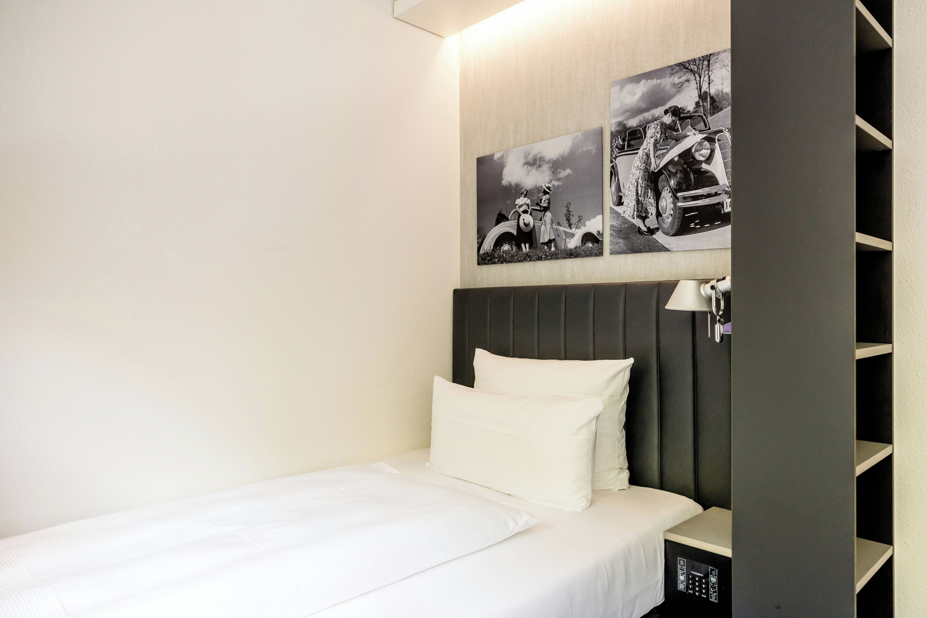 Une chambre d’hôtel avec un lit, une table de chevet, une lampe et deux photographies en noir et blanc accrochées au mur.