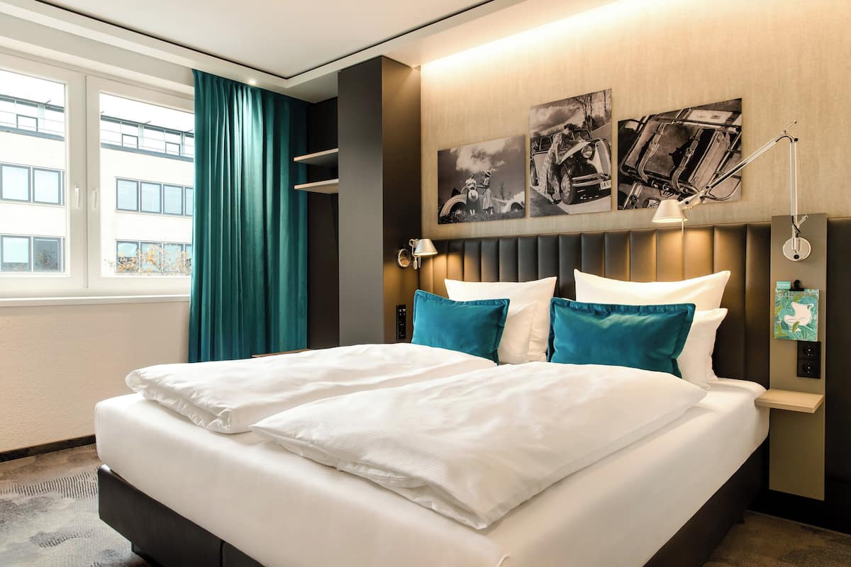Una habitación de hotel con una cama grande, cortinas color turquesa y obras de arte en la pared.
