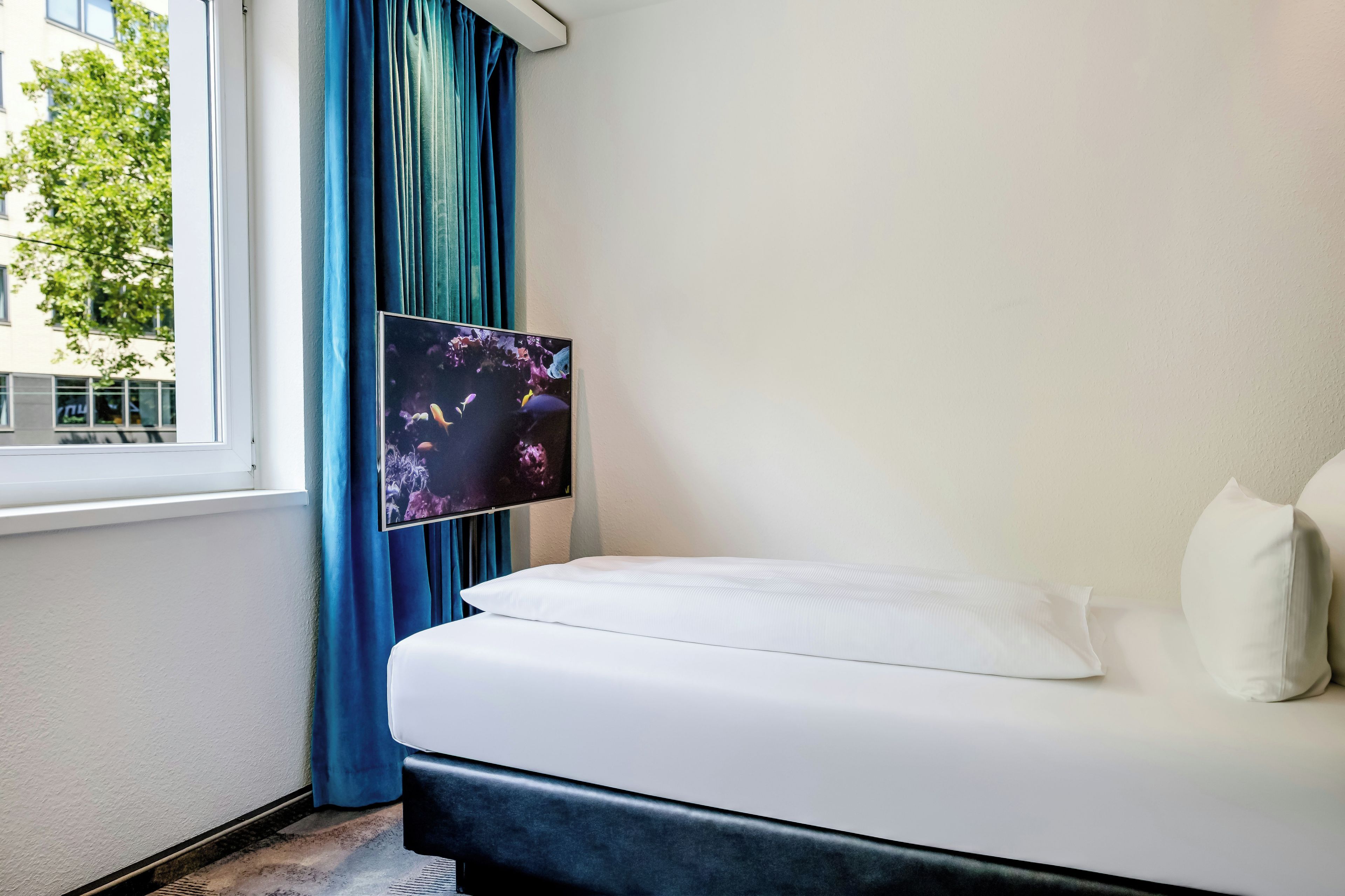 A hotel room with a bed, a window, and a wall-mounted TV.