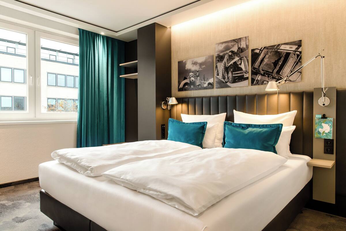 Una habitación de hotel con una cama grande, cortinas color turquesa y obras de arte en la pared.