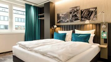 Een hotelkamer met een groot bed, blauwgroene gordijnen en kunst aan de muur.
