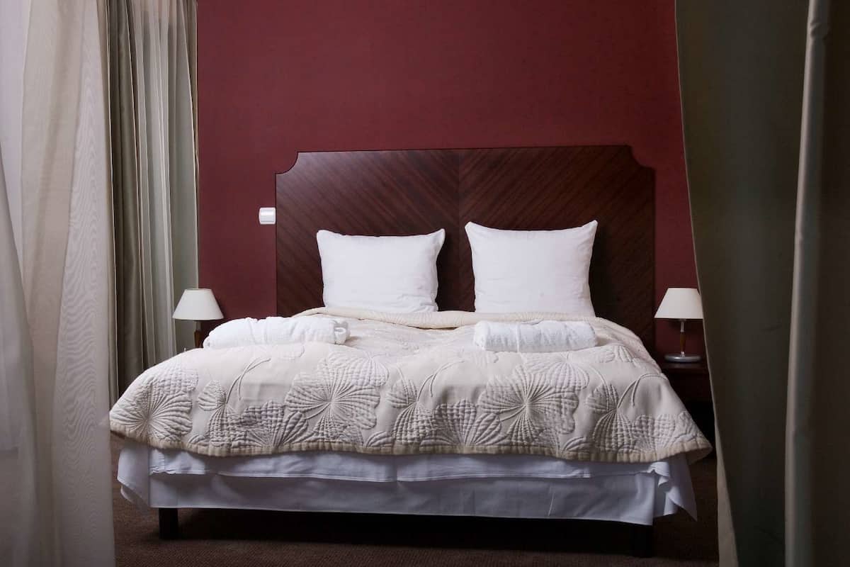 A neatly made bed with a white comforter and pillows, two bedside lamps, and a wooden headboard.