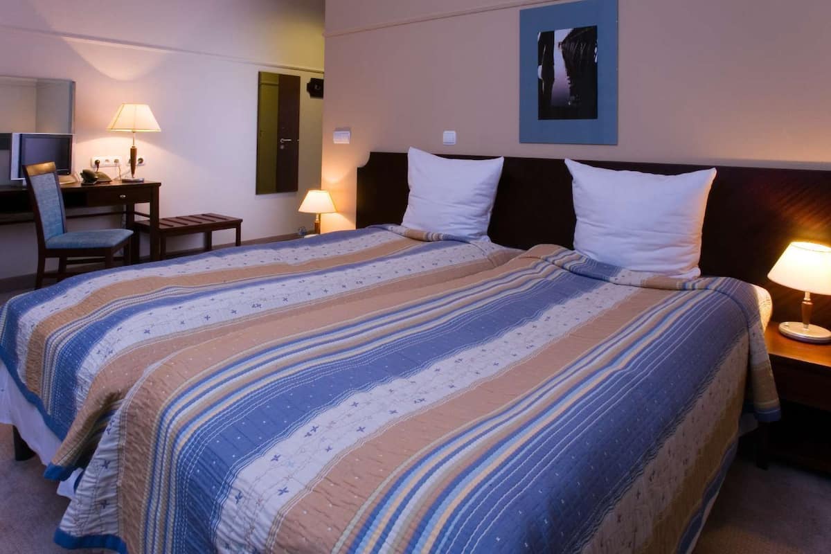 A hotel room with a large bed, two bedside lamps, a desk with a chair, and a mirror.