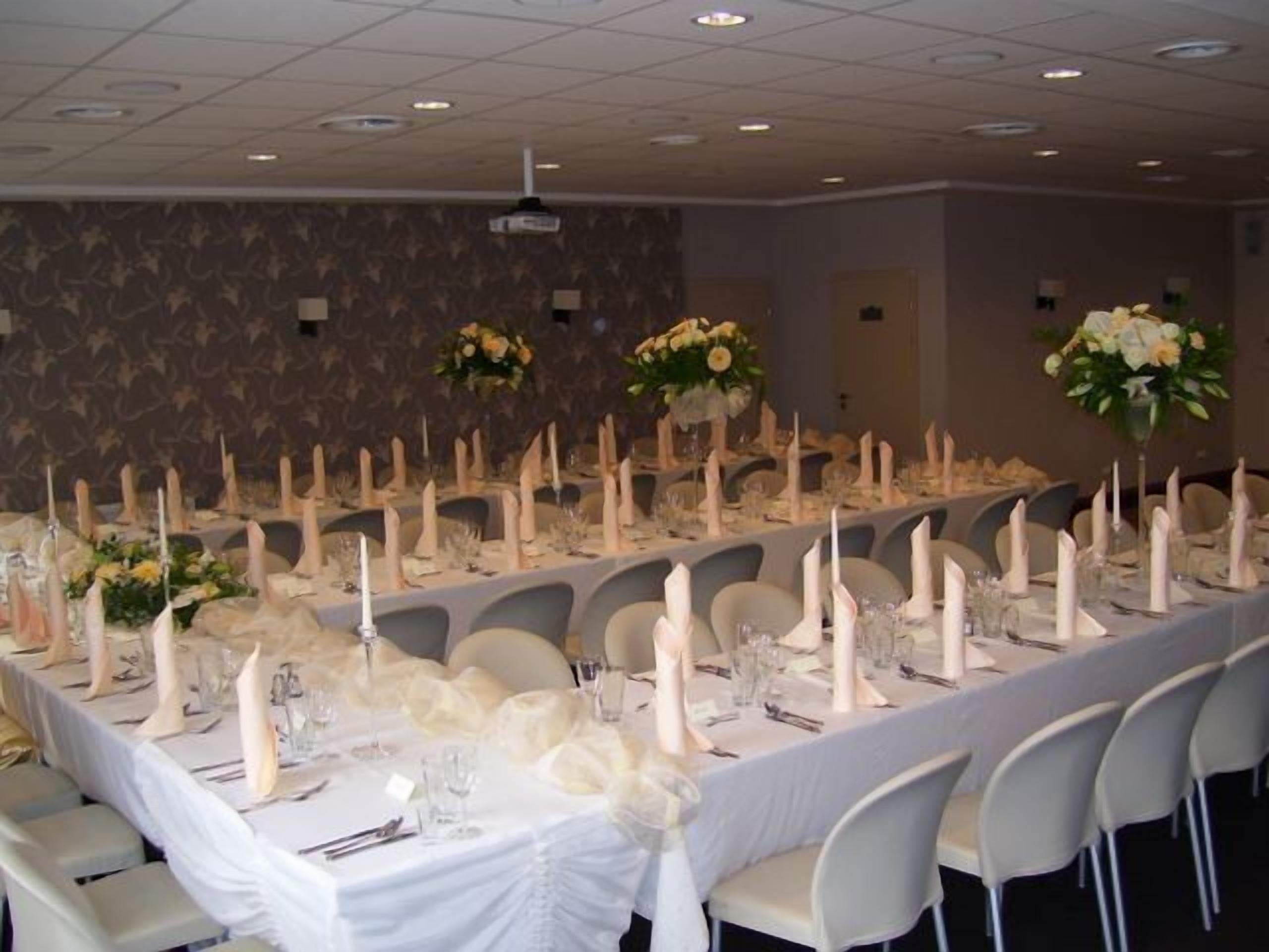 Un salón de banquetes con largas mesas dispuestas para un evento formal, que incluye manteles blancos, velas y centros de mesa florales.