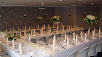 Un salón de banquetes con largas mesas dispuestas para un evento formal, que incluye manteles blancos, velas y centros de mesa florales.