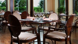 A restaurant with wooden tables and chairs, large windows with a view of greenery, and a modern interior design. - Hotel Kuracyjny (Gdynia)