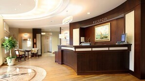 A reception area with a wooden reception desk, a painting, and a potted plant. - Hotel Kuracyjny (Gdynia)