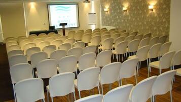 Una sala de conferències amb files de cadires blanques, una pantalla de projecció i un atril.