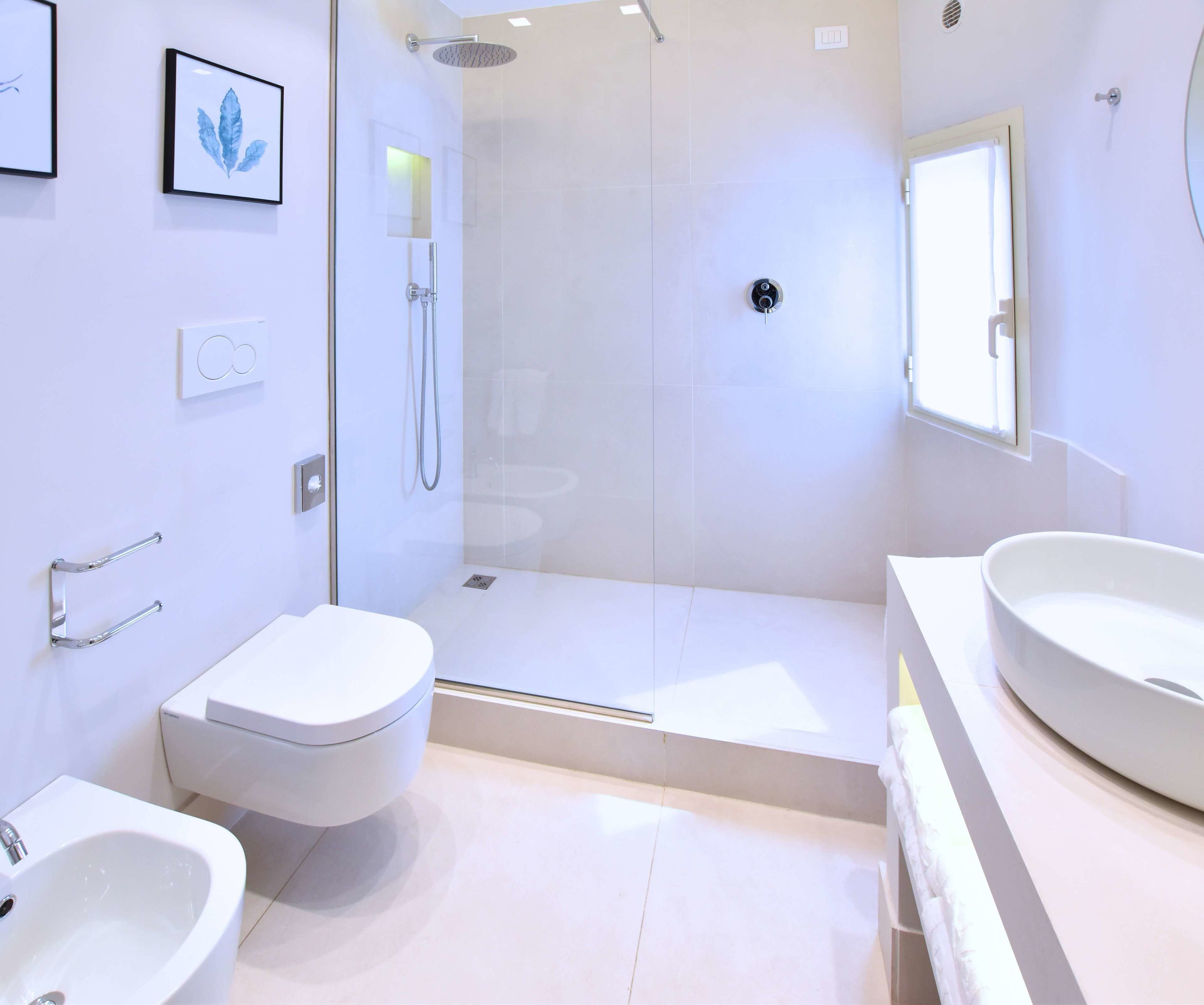 A modern bathroom with a glass-enclosed shower, a toilet, and two sinks.