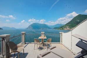 A balcony with a table and chairs overlooking a body of water, with mountains in the background.