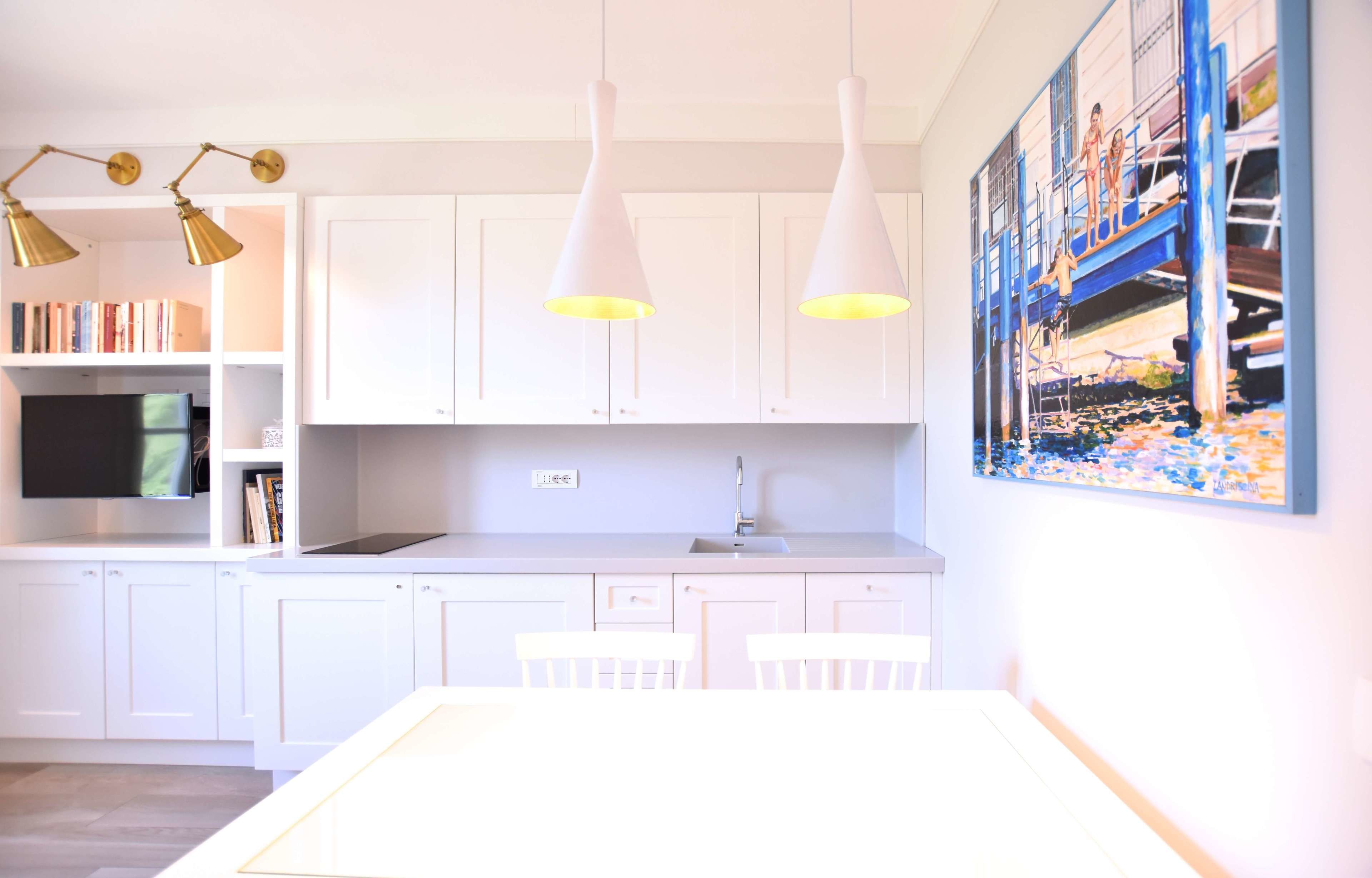 Una cocina moderna con armarios blancos, horno empotrado y luces colgantes.