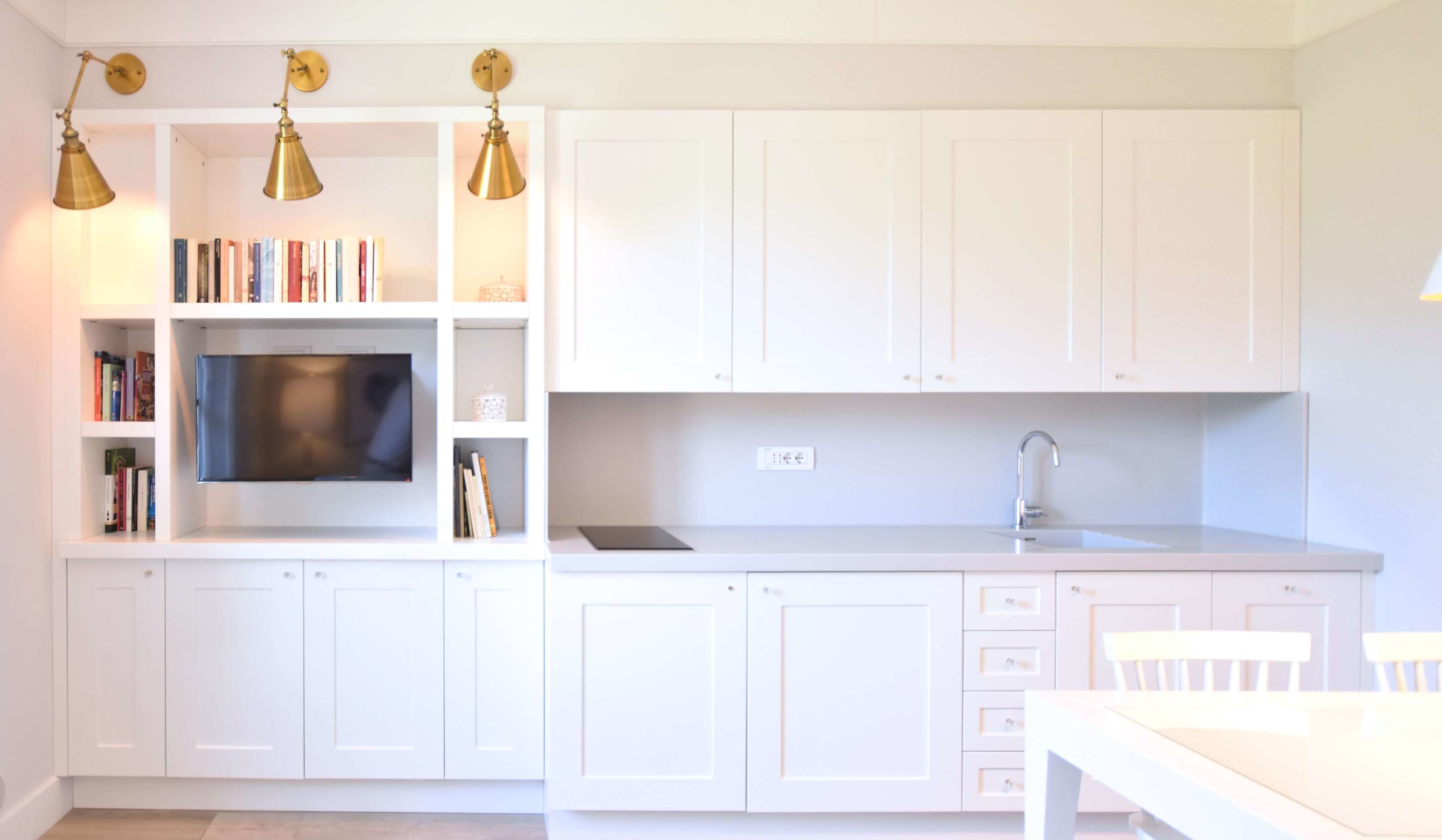 Una cocina moderna con armarios blancos, televisor integrado y lámparas colgantes.