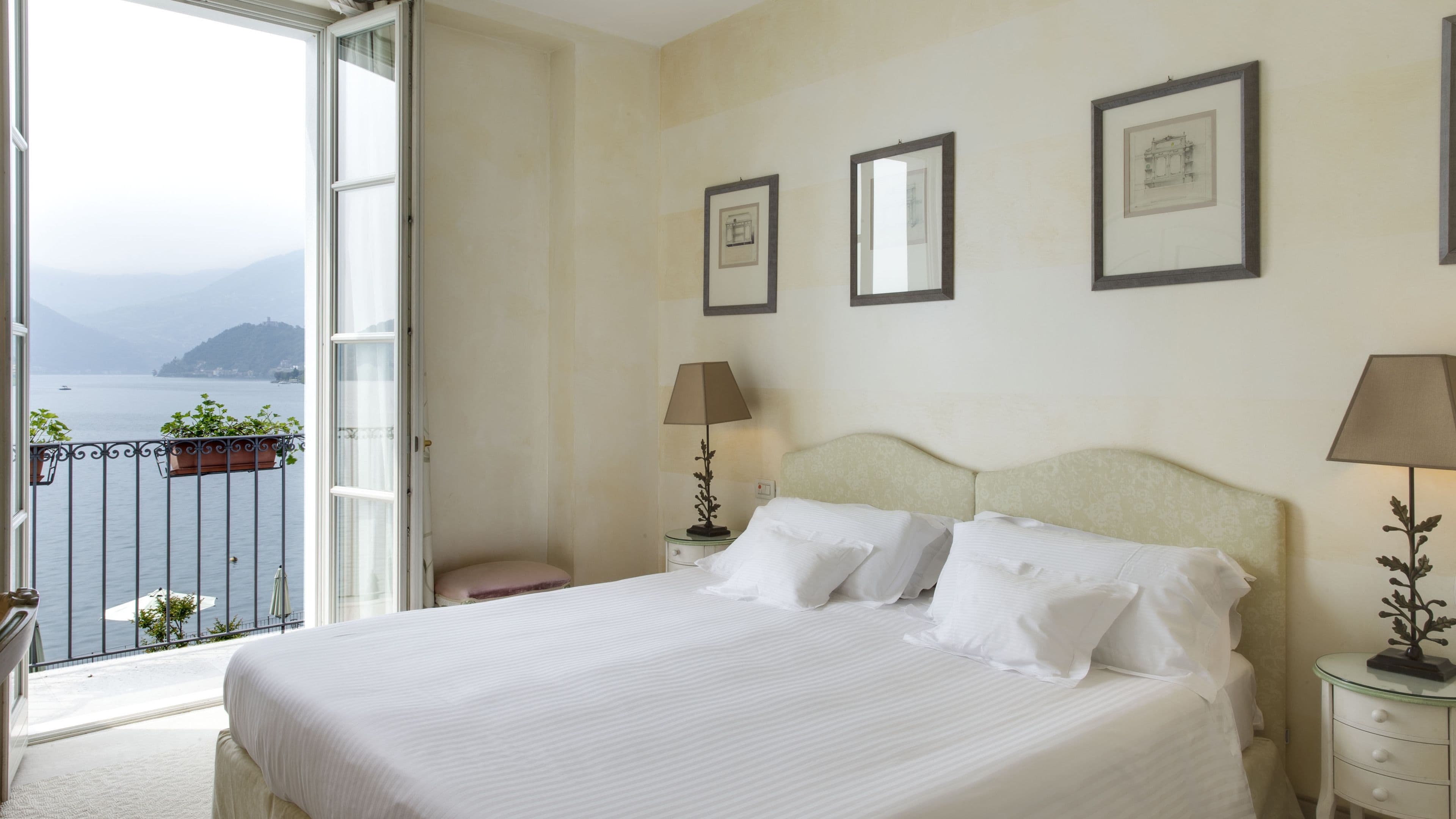 A hotel room with a bed, two bedside tables, a window with a view of the sea, and framed pictures on the wall.