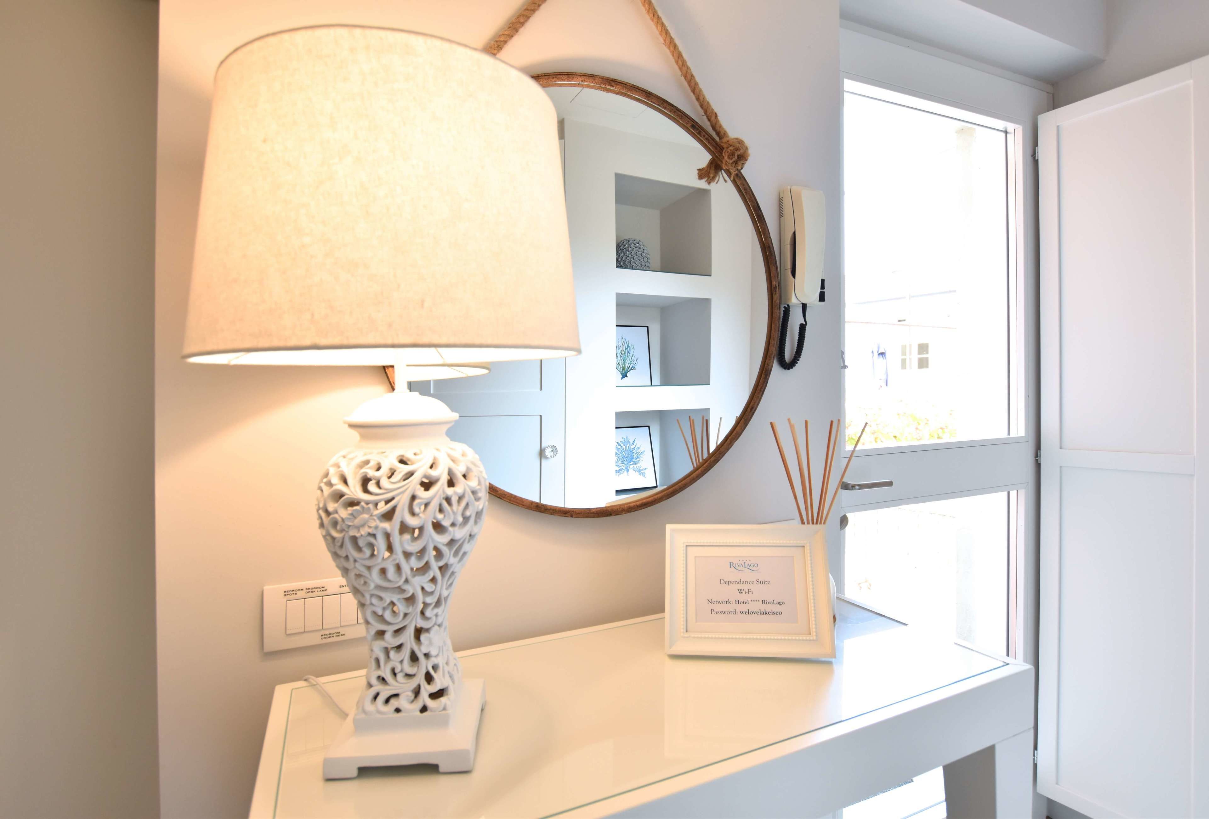 A white table with a decorative lamp, a framed sign, and a mirror with a rope handle.
